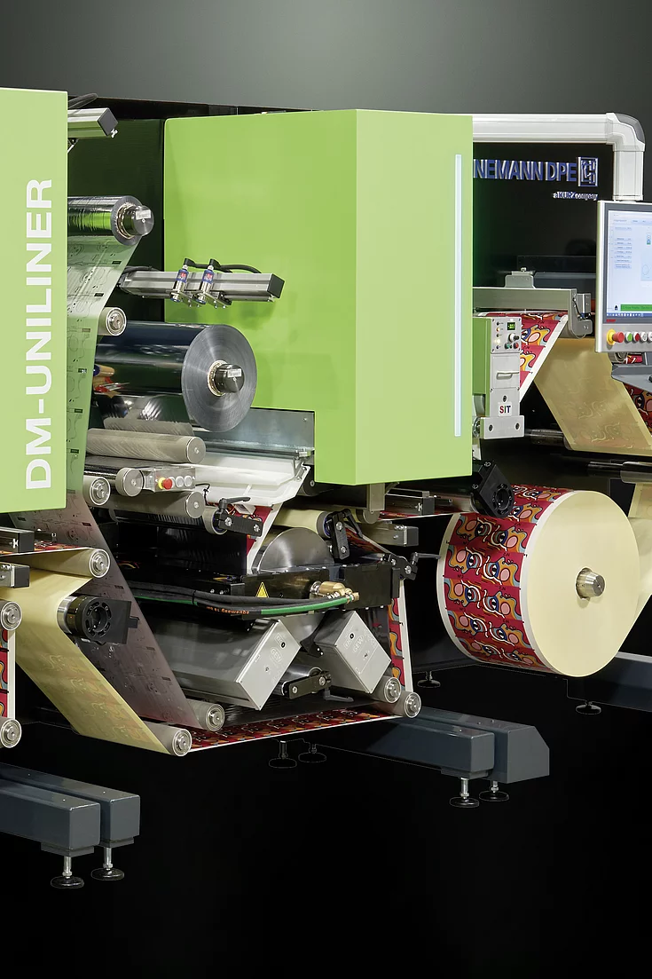 Digital Embellishment Solution with green panels, multiple rollers, two screens, and roll-fed colorful label material.